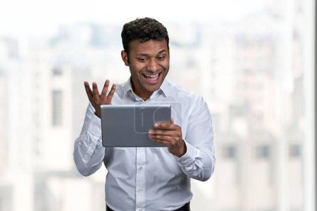 Téléchargez les photos : Incroyable jeune homme d'affaires heureux regardant tablette numérique pc. Joyeux jeune homme ayant appel vidéo. - en image libre de droit