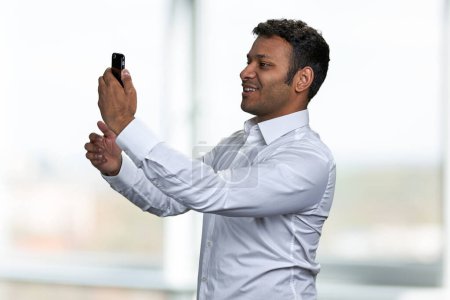 Photo for Handsome Indian man taking photo with mobile phone. Young man having video call with smartphone. - Royalty Free Image