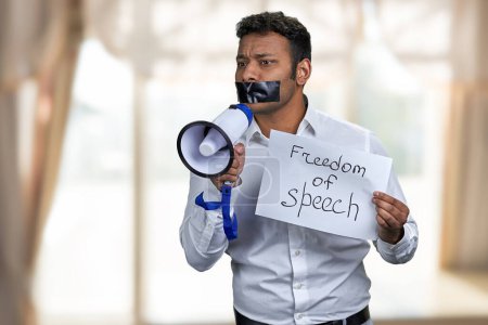 Téléchargez les photos : Jeune homme à bouche fermée essayant de parler en mégaphone. Concept de liberté d'expression. - en image libre de droit