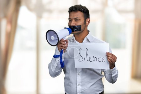 Photo for Indian man with taped mouth holding poster with inscription Silence. Censored male protester with megaphone. Freedom of speech. - Royalty Free Image