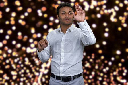 Téléchargez les photos : Jeune homme d'affaires indien attrayant travaillant sur une interface invisible. Festive bokeh lumières en arrière-plan. - en image libre de droit
