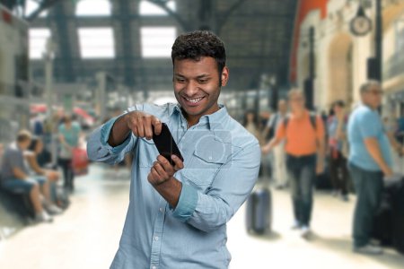 Foto de Joven alegre palying juego en su teléfono inteligente. Blur fondo de la estación de tren con personas que caminan. - Imagen libre de derechos