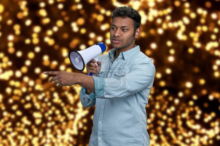 Photo for Young indian man talking into megaphone and pointing with index finger. Festive bokeh lights in the background. - Royalty Free Image