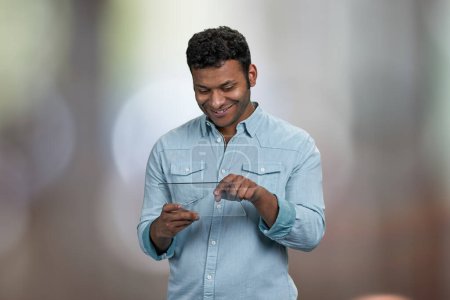 Téléchargez les photos : Jeune homme souriant utilisant une tablette numérique transparente. Résumé fond bokeh. - en image libre de droit