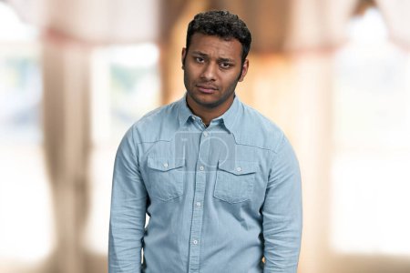 Photo for Portrait of upset young indian man looking at camera. Disappointed guy on blur interior background. - Royalty Free Image