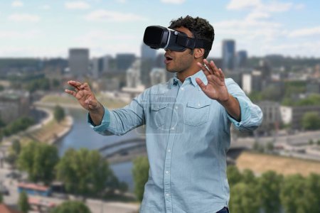 Photo for Young shocked man wearing vr glasses outdoor. Blur city skyscrapers in the background. Scared surprised man wearing vr headset. - Royalty Free Image
