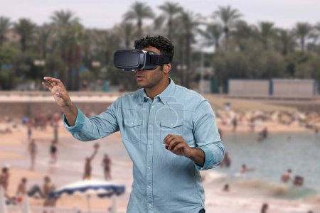 Foto de Guapo indio con gafas de realidad virtual. Blur piscina con turistas y palmeras en el fondo. - Imagen libre de derechos