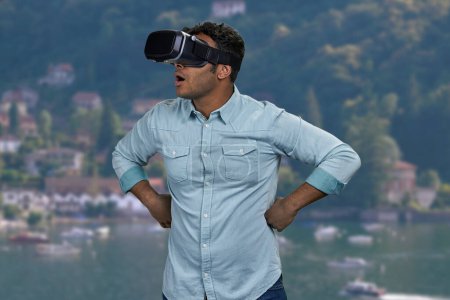 Téléchargez les photos : Surpris jeune homme portant des lunettes de réalité virtuelle. Flou mer et montagnes en arrière-plan. - en image libre de droit