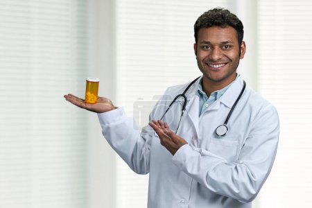Téléchargez les photos : Jeune médecin indien avec stéthoscope présentant des pilules sur fond de clinique floue. Médecine et concept de santé. - en image libre de droit