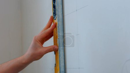 Foto de Un especialista dibuja marcas en la pared. Se trazan líneas para la fijación futura. - Imagen libre de derechos