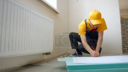 Photo for The worker draws a diagram on paper and on the walls. Repair in the house. - Royalty Free Image