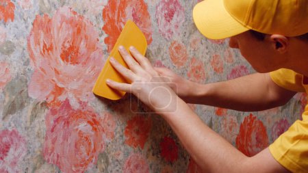 Téléchargez les photos : Builder lisse le papier peint avec une spatule. Réparation dans la maison. - en image libre de droit