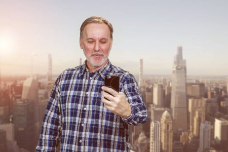 Photo for Happy smiling cheerful mature man is using his smartphone. Urban cityscape background. - Royalty Free Image