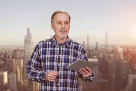Portrait of aged elder man with tablet pc device. Evening cityscape background.