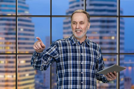 Photo for Portrait of cheerful aged man with tablet pc. Checkered night cityscape background. - Royalty Free Image