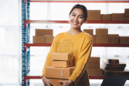 Photo for A beautiful Asian business owner opens an online store, she is checking orders from customers, sending goods through a courier company, concept of a woman opening an online business. - Royalty Free Image