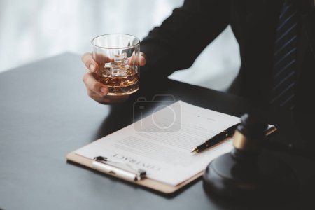 Un abogado sosteniendo un vaso de whisky, está en su oficina, y está estresado por discutir por un cliente, es un abogado. Concepto de litigio jurídico claro.