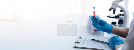 Photo for Lab assistant, a medical scientist, a chemistry researcher holds a glass tube through the blood sample, does a chemical experiment and examines a patient's blood sample. Medicine and research concept. - Royalty Free Image