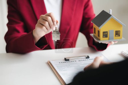 Téléchargez les photos : A home rental company employee is handing the house keys to a customer who has agreed to sign a rental contract, explaining the details and terms of the rental. Home and real estate rental ideas. - en image libre de droit