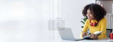 American teenage woman sitting in white room with laptop, she is a student studying online with laptop at home, university student studying online, online web education concept. Poster 651413834