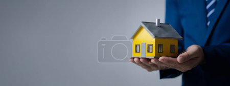 Photo for Person puts her hand on top of a miniature house model, photo of home insurance concept, when buying a new home should have home insurance to be sure if there is any danger to the home. - Royalty Free Image