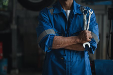 Photo for Car mechanic in uniform holding wrench at auto workshop, all kinds of auto specialists, expert auto repair and accredited auto repair centers. - Royalty Free Image