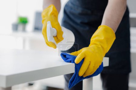 Photo for Person cleaning the room, cleaning staff is using cloth and spraying disinfectant to wipe the tables in the company office room. Cleaning staff. Maintaining cleanliness in the organization. - Royalty Free Image