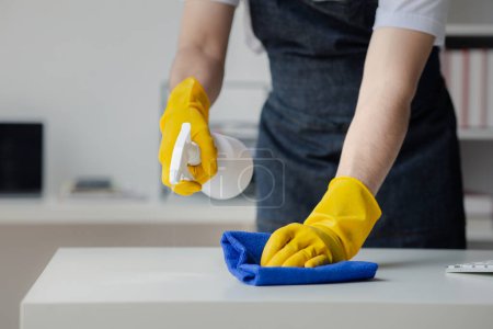 Photo for Person cleaning the room, cleaning staff is using cloth and spraying disinfectant to wipe the tables in the company office room. Cleaning staff. Maintaining cleanliness in the organization. - Royalty Free Image