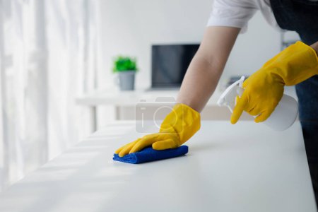 Photo for Person cleaning the room, cleaning staff is using cloth and spraying disinfectant to wipe the desk in the company office room. Cleaning staff. Maintaining cleanliness in the organization. - Royalty Free Image