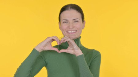 Téléchargez les photos : Young Woman with Heart by Hands on Yellow Background - en image libre de droit