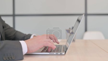 Téléchargez les photos : Vue latérale de l'homme d'affaires tapant sur ordinateur portable - en image libre de droit