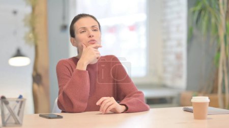 Mujer joven pensativa pensando mientras está sentada en el trabajo