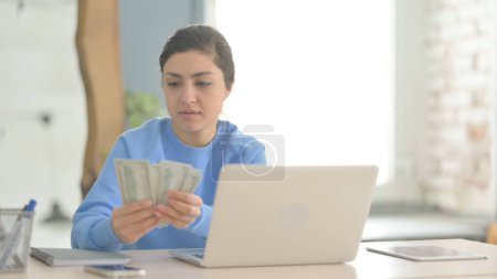 Téléchargez les photos : Femme indienne compte dollar tout en travaillant sur ordinateur portable - en image libre de droit