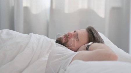 Foto de Vista lateral del hombre joven adulto que se despierta y deja la cama - Imagen libre de derechos