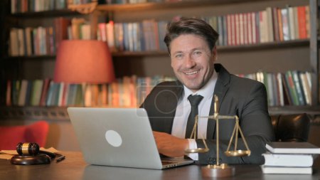 Téléchargez les photos : Sourire avocat masculin regardant la caméra tout en travaillant sur ordinateur portable - en image libre de droit