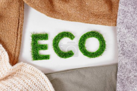 Téléchargez les photos : Concept de vêtements produits dans le respect de l'environnement avec texte "ECO" fait d'herbe entourée de textiles - en image libre de droit