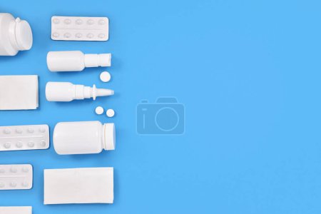 Medication for cold and flue. Nasal spray, throat spray, pills and tissues on blue background with copy space