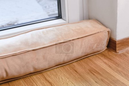 Téléchargez les photos : Draft excluder lying in front of door to keep out cold air and save energy for heating in room - en image libre de droit