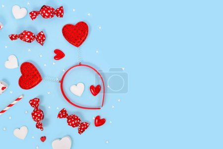 Valentine's Day flat lay with heart ornaments, headband and candy on blue background with copy space