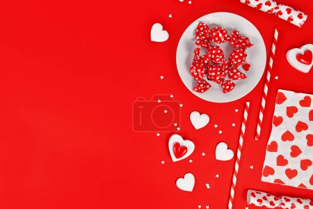 Valentinstag Dekoration mit Süßigkeiten, Herzschmuck und Zuckerstreusel auf rotem Hintergrund mit Kopierraum