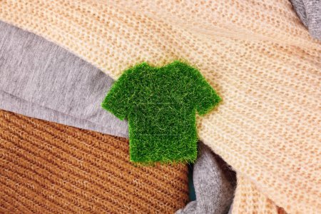 Konzept für umweltfreundlich produzierte Kleidung mit Hemd aus Gras umgeben von Pullovern