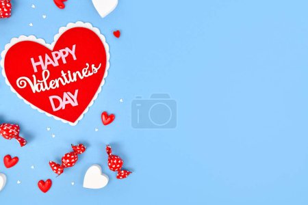 Valentine's Day flat lay with heart with text 'Happy Valentine's Day' and heart ornaments on blue background with copy space