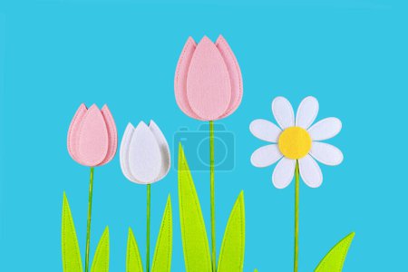 Felt tulip and daisy spring flowers on side of blue background