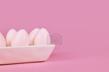 Simple one colored Easter eggs in egg tray on pink background with copy space
