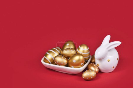 Golden Easter eggs painted with stripes and dots and bunny on red background with copy space