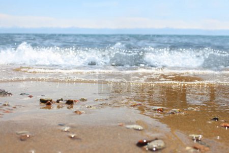 Téléchargez les photos : Defocused beach with blurred wave and wet sand with pebble on blue sky. Sea, ocean background. Vacation outdoor and travel holiday adventure concept - en image libre de droit