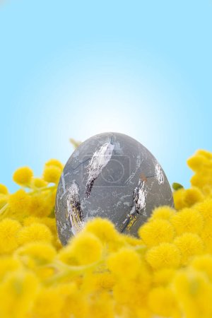 Foto de Painted gray egg with silver smears in yellow mimosa. Vertical. Easter. Copy space - Imagen libre de derechos
