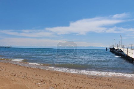 Foto de Paisaje marino con muelle gris de madera que conduce al mar, océano, lago con cielo azul. Concepto de viaje, paisaje marino, naturaleza. Issyk-Kul, Kirguistán. Copiar espacio - Imagen libre de derechos