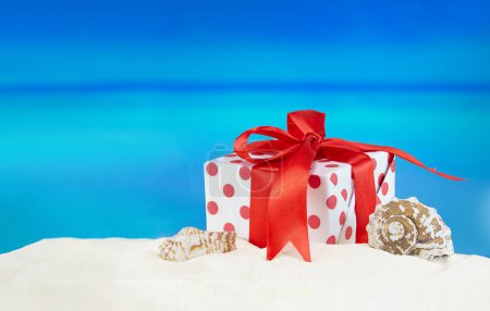 Foto de Caja regalo blanco-roja con lunares con lazo en la playa de arena con estrellas de mar y concha. Venta. Navidad, Año Nuevo, cumpleaños. Vacaciones en países calientes. Copiar espacio - Imagen libre de derechos