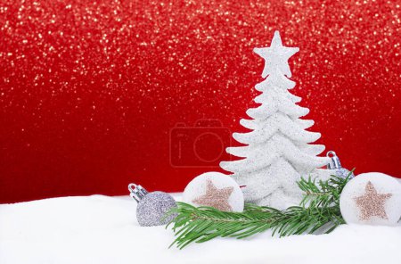 Téléchargez les photos : Arbre de Noël blanc brillant avec des boules d'argent et des étoiles avec une branche de pin sur le côté de la neige, derrière un fond rouge brillant. Nouvel An. Espace de copie - en image libre de droit